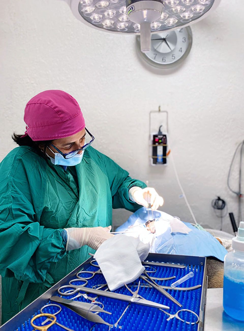 A surgeon in green scrubs operates on a patient, with surgical tools and a bright overhead light.